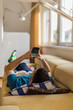 © qunica.com - Guy looking at his phone while lying on his sofa