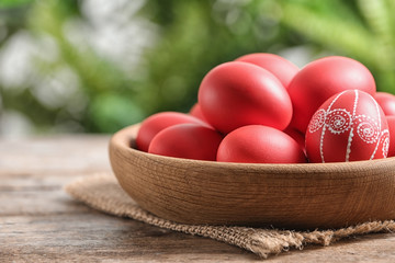 Wall Mural - Wooden bowl with red painted Easter eggs on table against blurred background, space for text