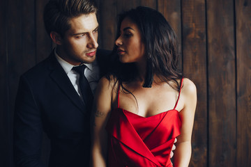 Wall Mural - Elegant man in a black suit. Couple at home. Hot woman in a red dress