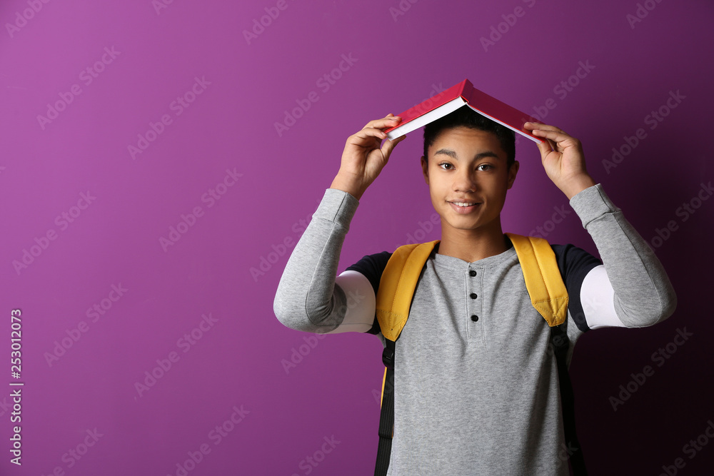 African-American schoolboy with book on color background