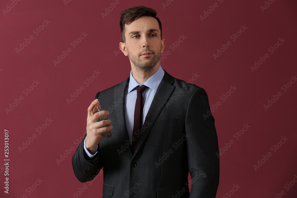 Handsome man with bottle of perfume on color background