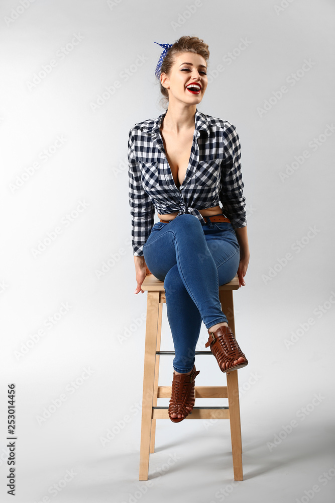 Beautiful pin-up woman sitting on stool against grey background