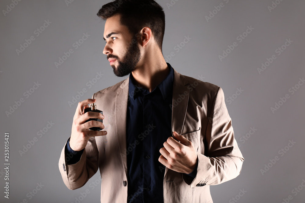 Handsome man with bottle of perfume on grey background