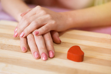 Wall Mural - Female hands and red heart on a wooden background.