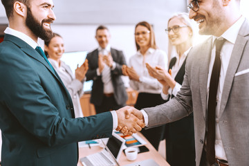 Two partners shaking hands while other colleagues clapping hands. We grow by lifting others.