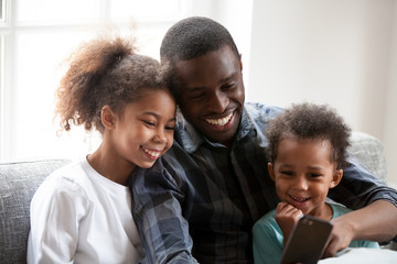 Wall Mural - Happy black dad play on smartphone with little daughters