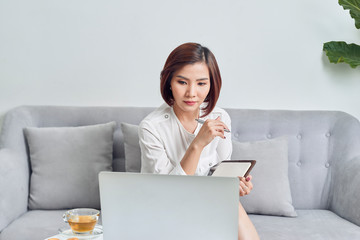 Asian woman in cafe using laptop and note some data on notepad