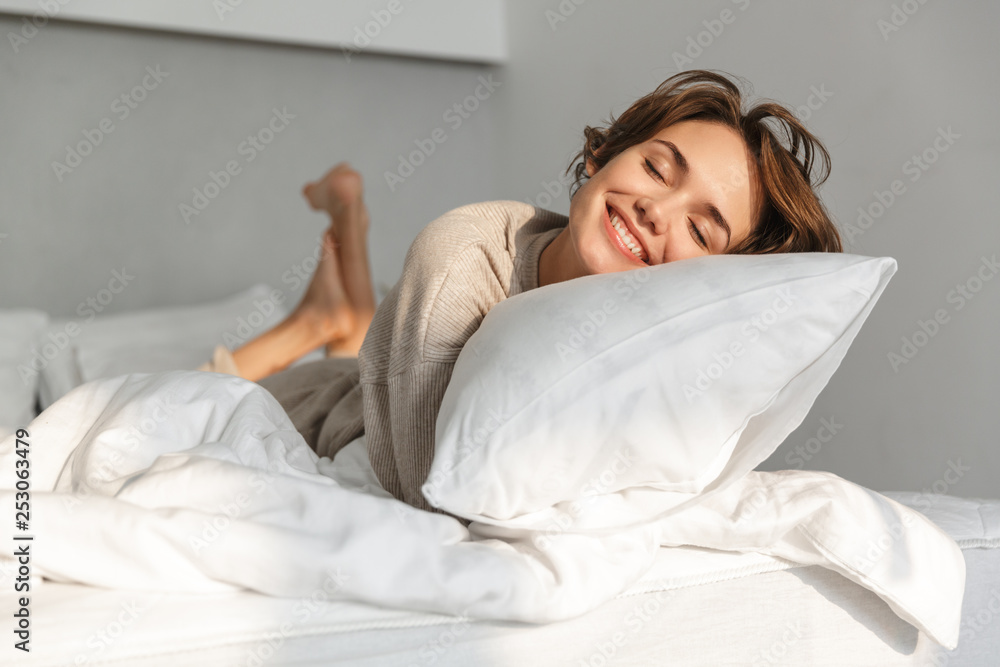 Smiling young girl relaxing in bed - obrazy, fototapety, plakaty 