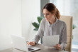 © fizkes - Serious focused businesswoman typing on laptop holding papers preparing report