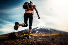 Young Woman, Trail Running Athlete Runs On The Trail With Loose Ground And Volcano On The Background. Tilt Shift Effect Applied