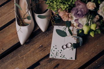 Wedding accessory bride. Stylish beige shoes, earrings, gold rings, flowers, garter on wooden background.