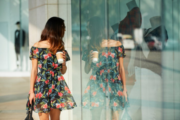 Elegant woman with cup looking at shop window