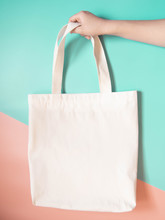 Blank White Tote Bag Canvas Fabric With Handle Mock Up Design. Close Up Of Woman Hand Holding Eco Or Reusable Shopping Bag On Green Orange Background. No Plastic Bag And Ecology Concept. Copy Space.