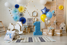 Birthday Gold And Silver Decorations With Gifts, Toys, Garlands And Figure For Little Baby Party On A White Bricks Background.