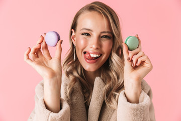 Poster - Happy cute young pretty woman posing isolated over pink wall background holding cake macaroons sweeties.