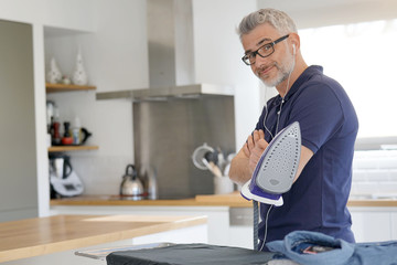 Poster - Mature man smiling holding iron in modern kitchen