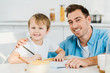 © LIGHTFIELD STUDIOS - father and preschooler son looking at camera and drawing during breakfast in kitchen