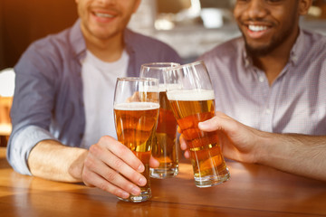 Wall Mural - Best friends clinking beer glasses in bar, closeup