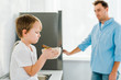 © LIGHTFIELD STUDIOS - sad boy holding bowl of cereal with disappointed father on background in kitchen