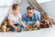 © LIGHTFIELD STUDIOS - father and preschooler son playing with toy cars and teddy bears under wigwam at home