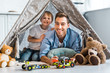 © LIGHTFIELD STUDIOS - happy father and preschooler son with toy cars and teddy bears looking at camera while sitting under wigwam at home