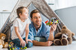 © LIGHTFIELD STUDIOS - father and preschooler son playing with toy car under wigwam at home