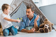 © LIGHTFIELD STUDIOS - surprised father looking at preschooler son playing with toy car under wigwam at home