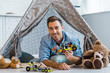 © LIGHTFIELD STUDIOS - handsome smiling man lying in wigwam, looking at camera and holding toy car in nursery