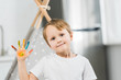 © LIGHTFIELD STUDIOS - adorable smiling preschooler boy with colorful paint on hand looking at camera at home