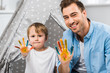 © LIGHTFIELD STUDIOS - happy father and son looking at camera and showing painted hands at home