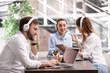 © New Africa - Young businessman with headphones, laptop and his colleagues at table in office