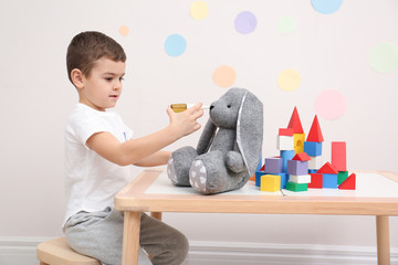 Wall Mural - Cute child playing doctor with stuffed toy at table in hospital