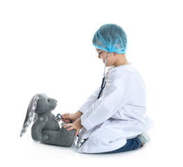 Wall Mural - Cute child playing doctor with stuffed toy on white background