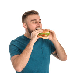 Wall Mural - Young man eating tasty burger on white background