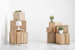© spaskov - Cardboard boxes of things are stacked on the floor against a white wall. Books and table lamps and green plants in pots. The concept of moving to a new home.