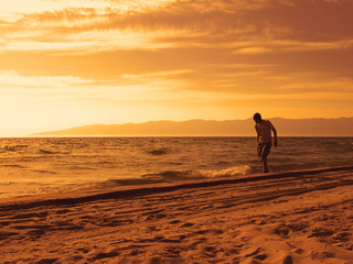 Alone young man walking on the beach barefoot in the evening. Sandy beach, mountains on the horizon, Sunset.