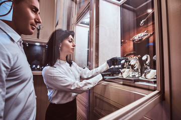 Seller shows the client an exclusive men's watch standing next to open showcase in the luxury jewelry store