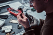 © Fxquadro - Electronic technician mending a broken phone, looking closely at the little bolt holding it with tweezers in the repair shop