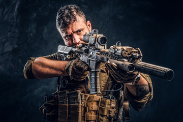 Wall Mural - Special forces soldier wearing body armor holding assault rifle and aim at the enemy. Studio photo against a dark textured wall