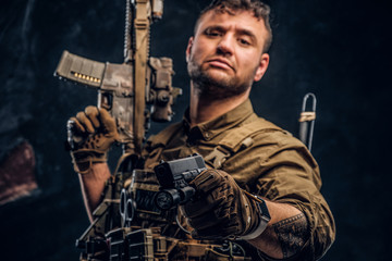 Wall Mural - Special forces soldier wearing body armor holding assault rifle and aiming a gun at the camera. Studio photo against a dark textured wall