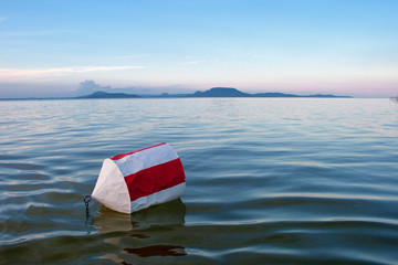 Wall Mural - Buoy with red and white stripes on the blue water of Lake Balaton with the Badacsony mountan in the background at sunset in Hungary