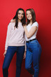 © Strelciuc - Portrait of a pretty young european girl smiling looking into camera leaning on her best girlfriend while that smiling is looking into camera against a red background.