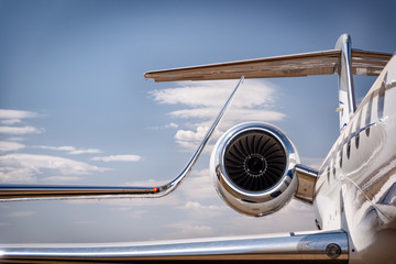 A winglet and engine of a luxury personal jet aircraft against a blue sky with cloud