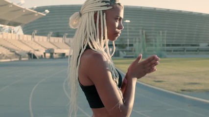 Wall Mural - African sportswoman with braided blond hair walking across the running track rubbing her hands. Female feeling cold during training session in stadium. 