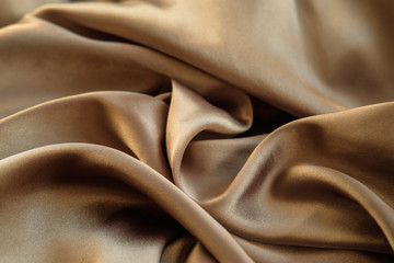 The gold fabric is laid out waves. Satin fabric. Brown material textile.
