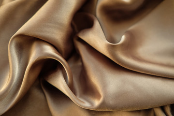 The gold fabric is laid out waves. Satin fabric. Brown material textile.