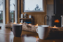 Pair Of Ceramic Glasses  In A Wooden Table With Candles In A Treetop Cabin With A Chimney And A Moody Look