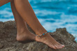 suntanned girl legs with boho style bracelet on right one, sits on seacliff,