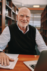 Wall Mural - Cheerful senior man learning sitting at a library