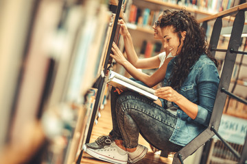 Wall Mural - Two female students read and learns by the book shelf at the library.Reading a book.